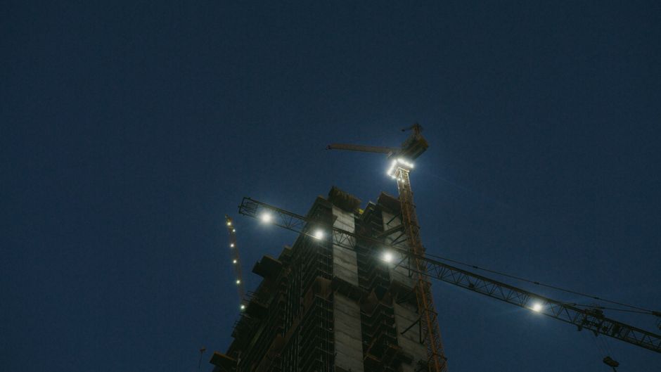 Podswietlony reflektorami LED zuraw wiezowy pracujacy na budowie w nocy